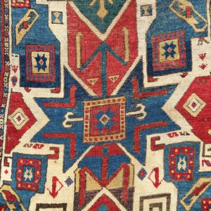 Detail of the antique early 19th century Caucasian Star Kazak rug, showing a blue star medallion surrounded by angular hooked motifs and stepped ivory outlines.